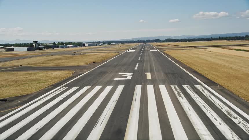 Low flying aerial footage of an airfield runway approaching the mountains in the horizon at Hillsboro Airport in Oregon showcasing the sunny daytime views during summer