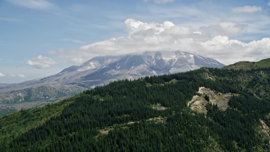 Aerial view approaching Mount St Helens with partly cloudy skies showcasing the majestic peaks of the Cascade Mountains in Washington during summer