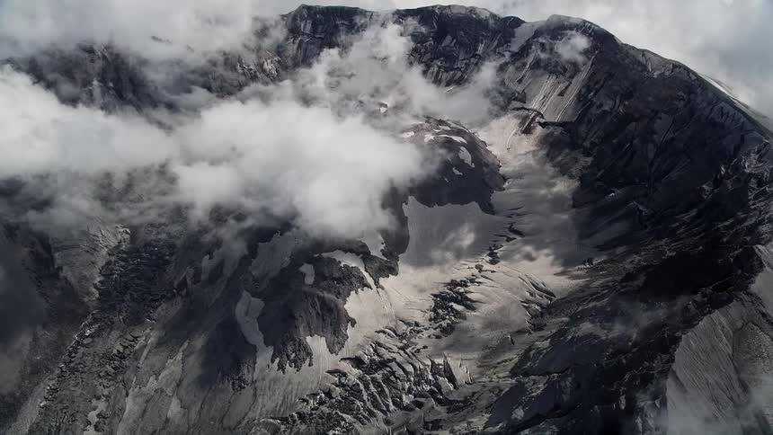 Approach the Mount St Helens crater by aerial view with low clouds and mist-covered rocky mountains during daytime in Washington