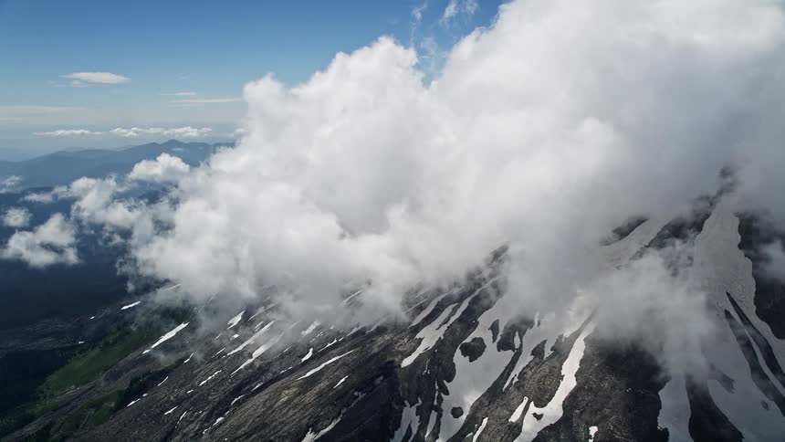 Aerial footage of Mount St Helens during summertime with snowy slopes and clouds passing by