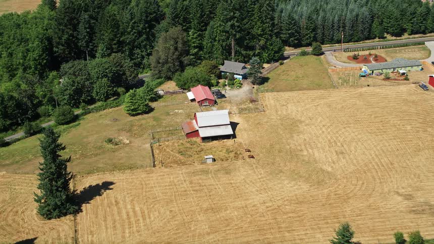 Aerial footage of an approach to a red barn surrounded by farm fields in La Center Washington on a sunny day in the Pacific Northwest during summer
