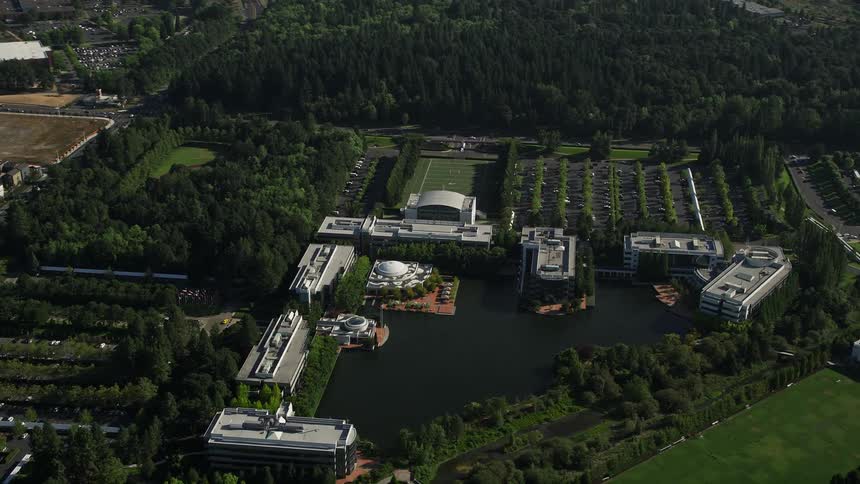 Aerial footage of Nike Headquarters in Beaverton Oregon surrounded by trees and beside a lake captured during a sunny day in the summer