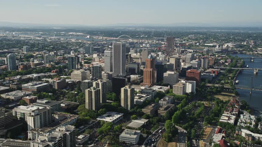 an aerial view of downtown Portland Oregon during summer showcasing the city's skyscrapers and high-rises as the camera approaches the metropolis under the warm sunshine