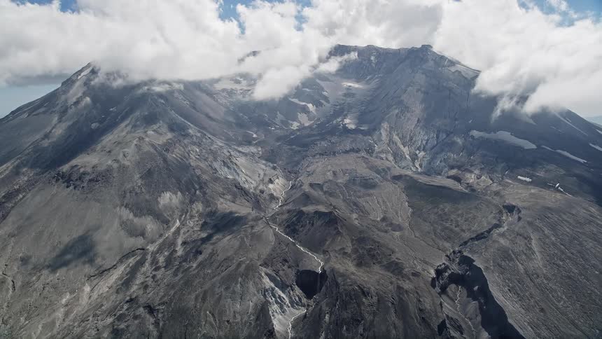 Aerial footage captures the clouds surrounding the summit of a massive mountain range in Washington during the summer