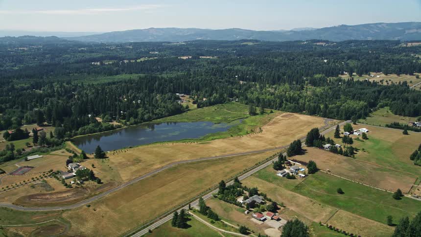 Aerial footage of picturesque farmlands and fields surrounding a serene pond in La Center Washington during a sunny summer day