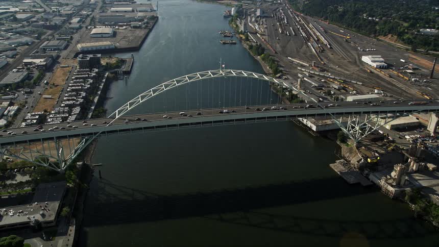 Aerial shot of the Fremont Bridge and Willamette River as a vehicle approaches and orbits the bridge showcasing the beauty of downtown Portland Oregon on a sunny day during the summer