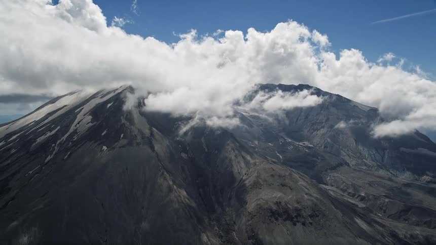 Aerial footage orbiting Mount St Helens with clouds and snow patches showcasing the majestic peaks of the Cascade Mountains in Washington during summertime