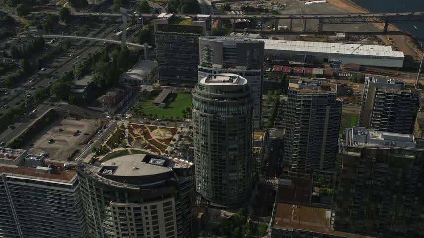 Aerial footage of Portland Oregon's South Waterfront neighborhood featuring skyscrapers near a river with a city park in the background during summer
