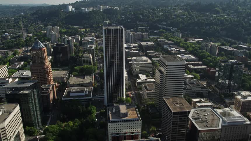 an aerial view of Downtown Portland Oregon as the camera tilts up from the Steel Bridge revealing towering skyscrapers and the beautiful Willamette River on a sunny day during summer