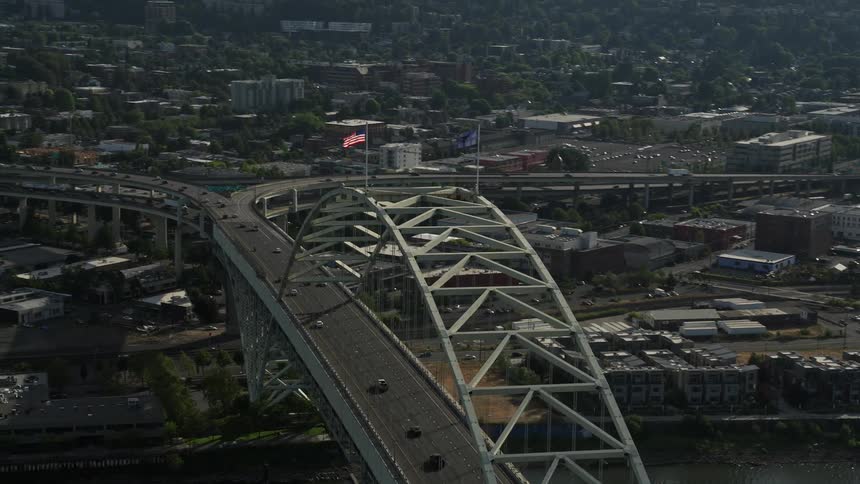 an aerial view of Downtown Portland Oregon during a sunny summer day with an American flag waving proudly atop a bridge revealing the stunning skyline of high-rises and skyscrapers