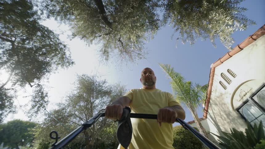 A man mowing the lawn as he sweat and wipe his face with an handkerchief