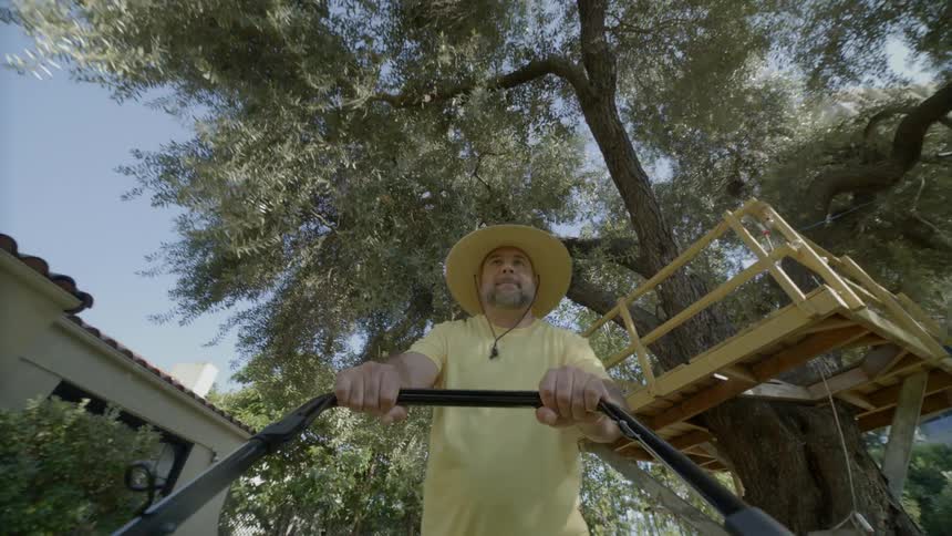 Man wearing a hat and a yellow shirt mowing a lawn during day time