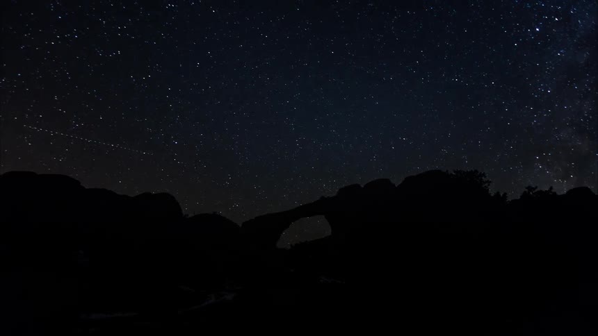 Stars and lights move in the sky above a rock formation