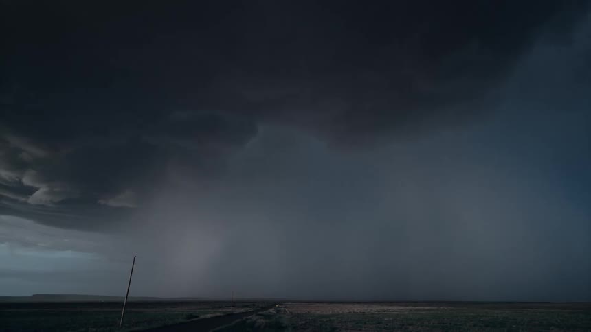 A supercell storm moves over a rural road pouring down rain as lightning strikes