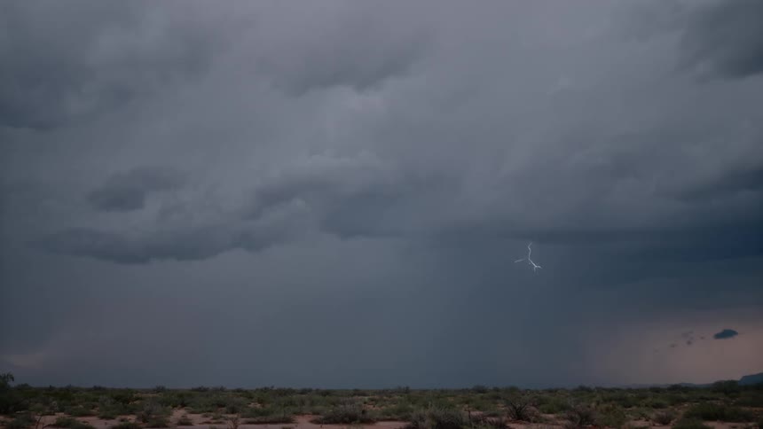 A cloudy gray sky with lightning striking down from the clouds across a flat grassland landscape