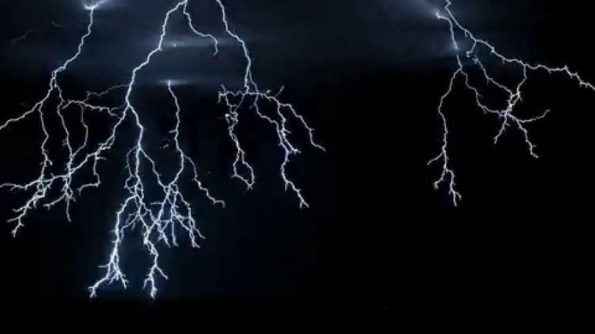 A lightning storm flashing in the dark night sky lighting up the ground and sky around it