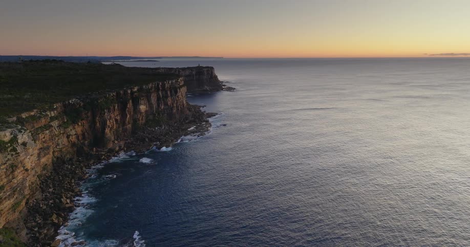 An aerial over the ocean coastline meeting a cliff face during dusk