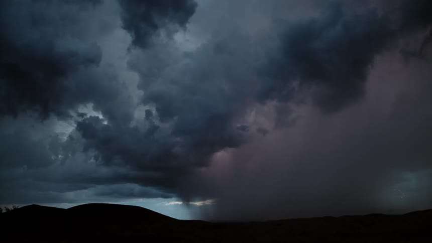 Dark storm clouds move over mountains pouring rain as lightning strikes the ground