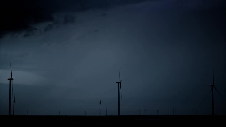 Dark storm clouds move over a wind farm as lightning strikes the ground