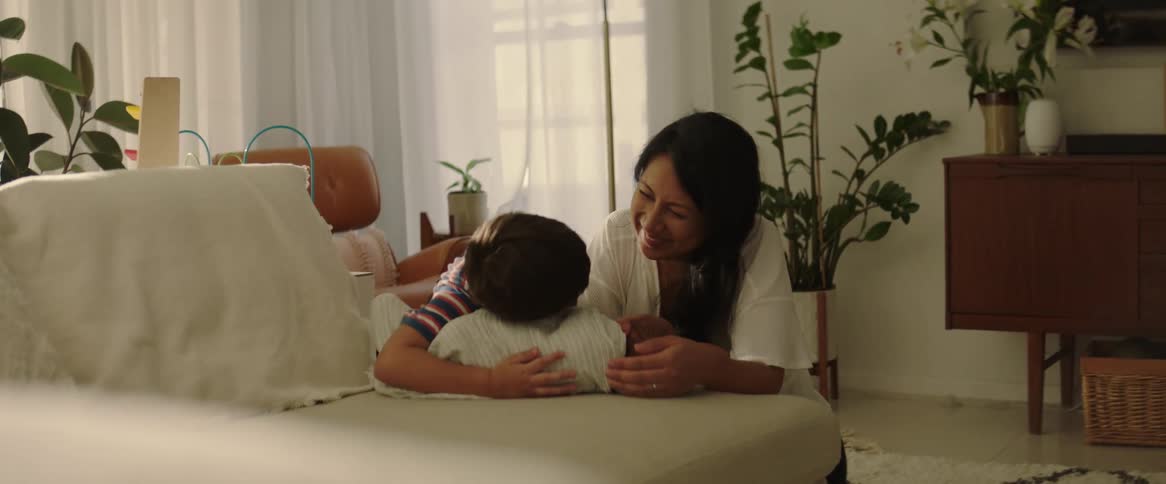 A mother sitting on the floor next to her young son as they hug and coddle a newborn baby on the couch