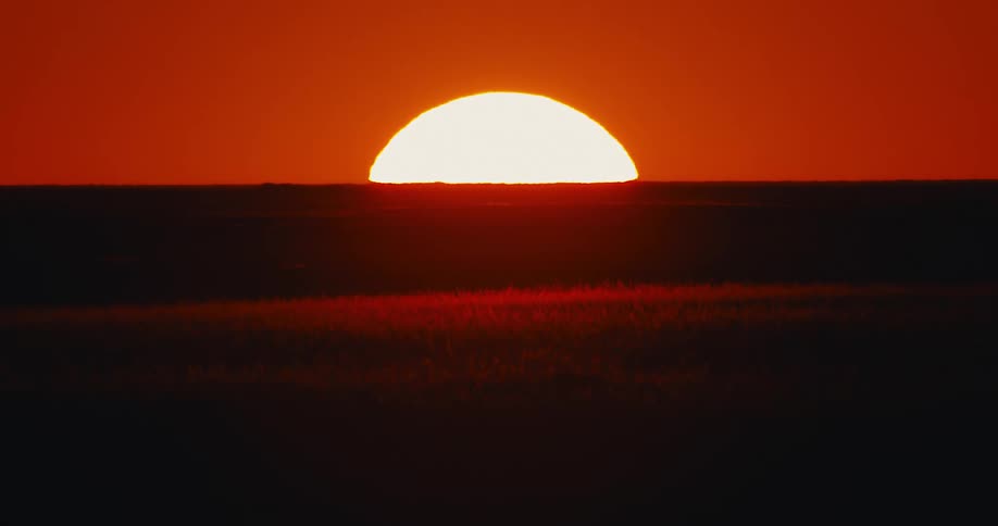 The view of the sun in the evening as it sets on a plain field