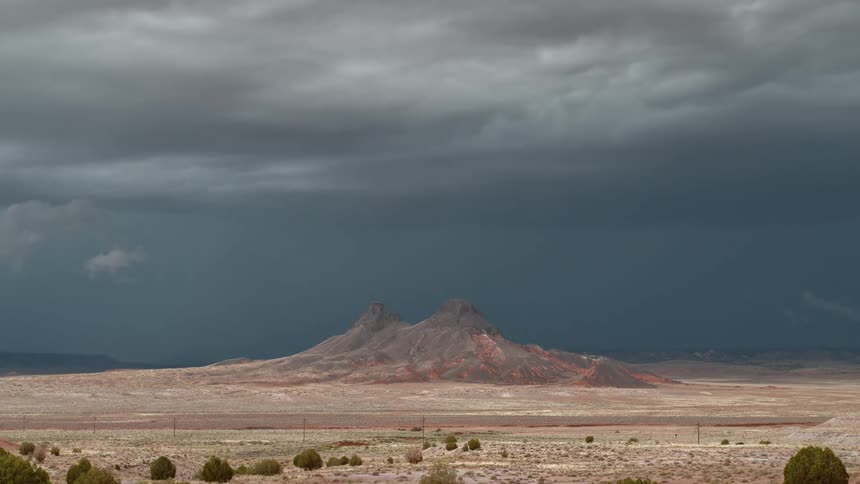 A wide open desert landscape with a small mountain range in the middle as lightning strikes down from the sky during a storm