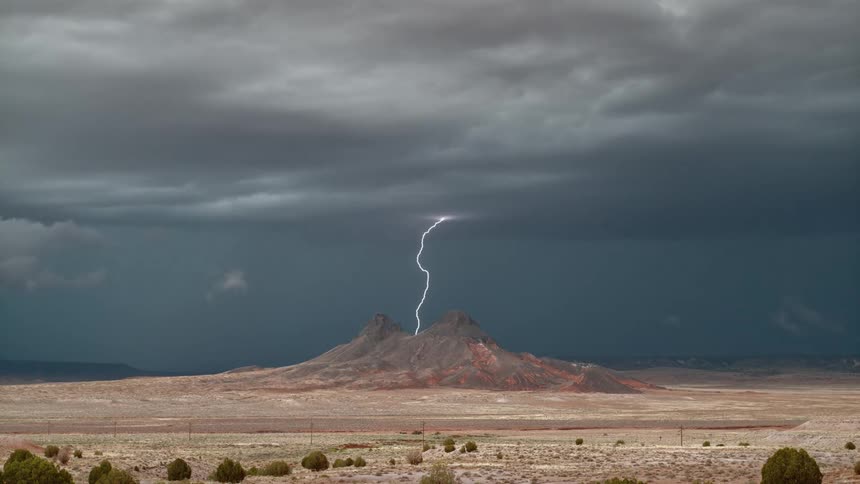 A wide open landscape with lightning striking down above a mountain peak