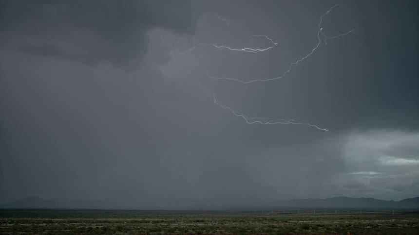 Lightning striking across a cloudy gray sky and hitting the ground across a prairie