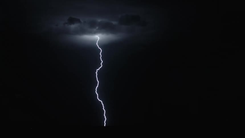 Bolts of lightning descend to the ground from dark storm clouds at night
