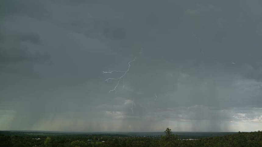 Lightning flashes and moves across the sky over a town and strikes the ground
