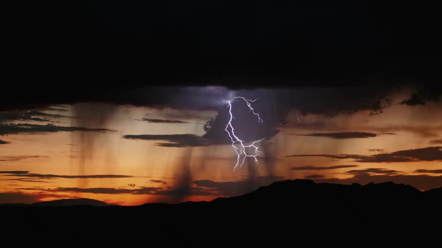 Lightning bolts striking across the sky during a storm hovering over the silhouette of mountains at dusk