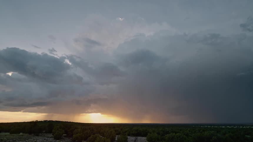Fluffy clouds hovering the sky as the sun sets behind them and lightning flashes across and strikes the sky