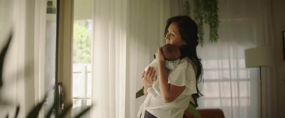 A mother holding her newborn baby as she stands in front of a window swaying back and forth