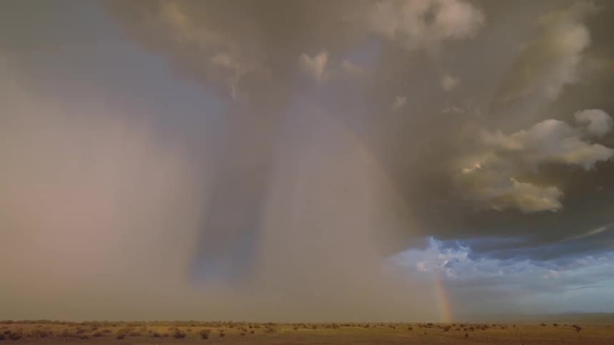 A lightning storm over a desert plain creating a rainbow