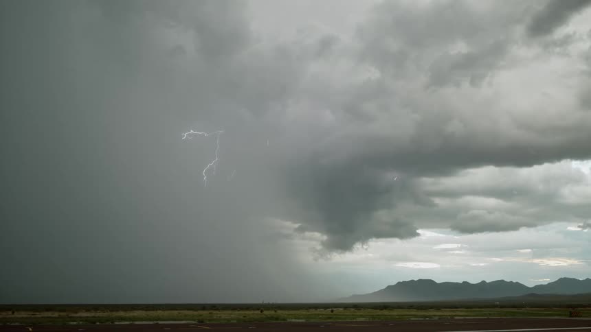 A cloudy storm with lightning striking from the clouds on a wide open landscape with mountains on the horizon