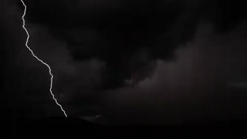 Lightning lighting up the dark night sky revealing storm clouds and mountain silhouettes
