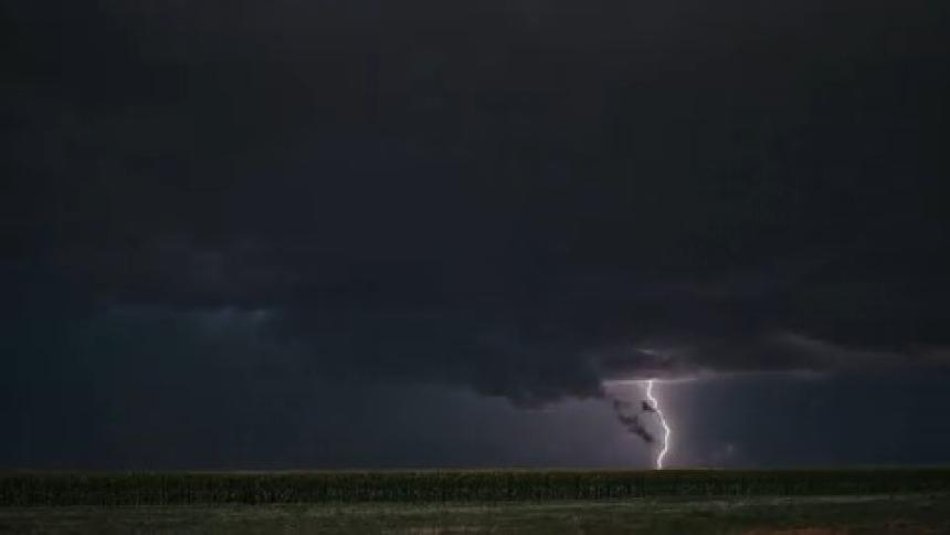Thunderstorm and lighting striking down across a wide open field landscape in the middle of the ngiht against a cloudy sky