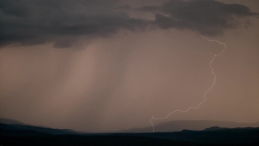 A lightning storm striking across the sky and down to the ground above silhouette mountains covered in fog