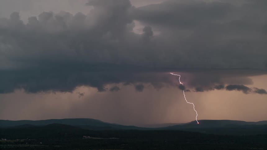 A cloudy gray sky with lightning striking down onto a mountain on the horizon landscape