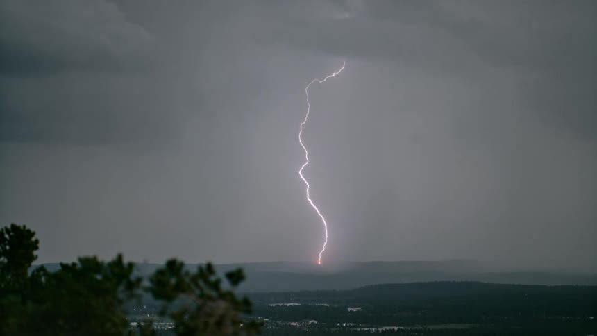 Lightning striking from the sky to the ground on a mountain landscape with dark clouds covering the sky