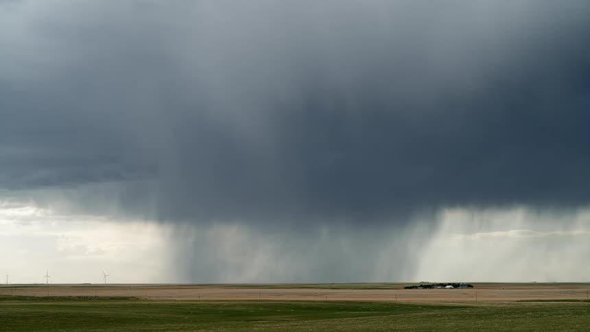 A supercell storm moves across rural land near a wind farm pouring down rain as lightning strikes