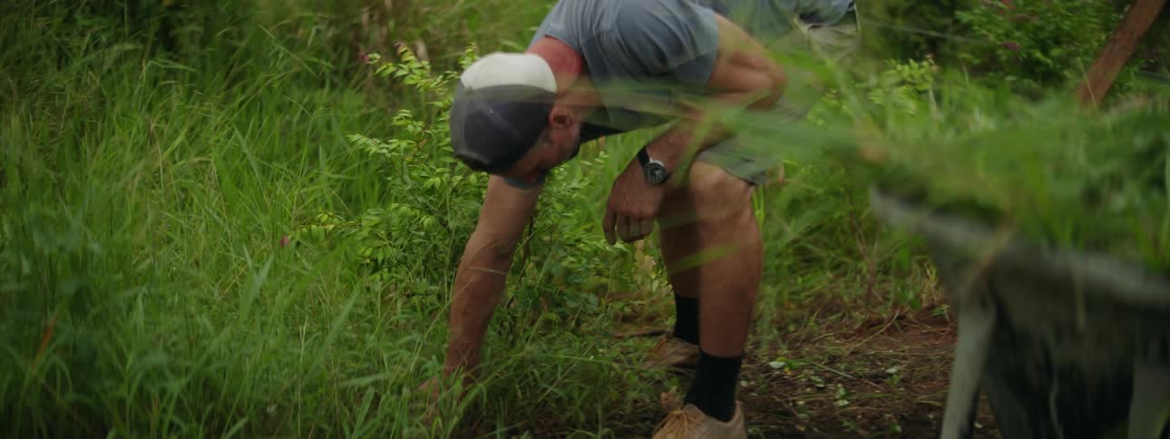 A amn wearing a cap in a grass field uprooting the grass with his hands