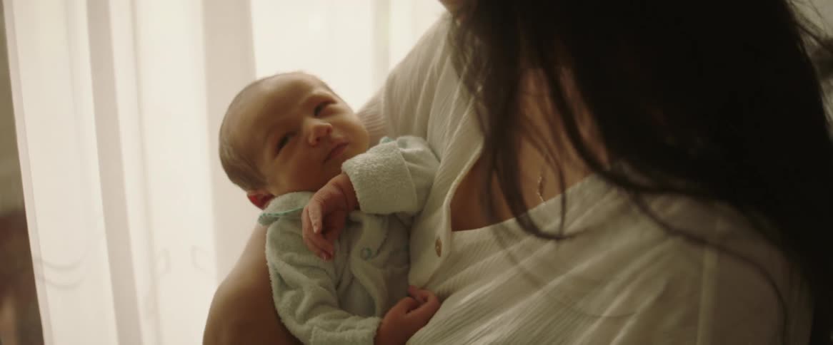 A mother holding a newborn baby in her arms swaying back and forth in front of a sunlit window