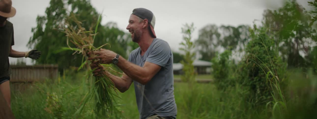 A man pulling weeds from his garden laughing and smiling as he puts them in a trash can