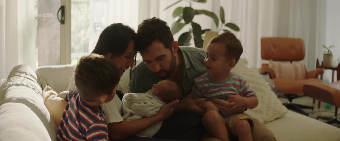 A couple and their two young boys welcome their new baby laughing and kissing