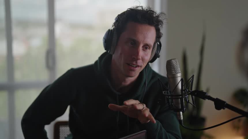 Man wearing headphones smiles while sitting in office and talking into microphone