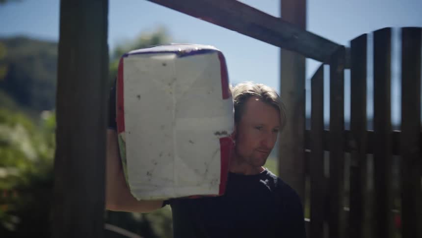 A man walked out of a wooden gate to drop the carton on his shoulder