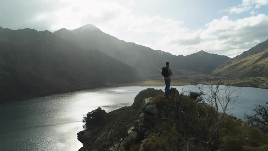 Man on top of a cliff overlooking the lake and mountains in the background