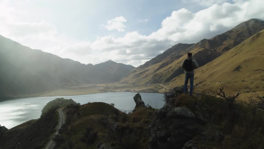 A man on top of a hill looking down on a river surrounded by mountains