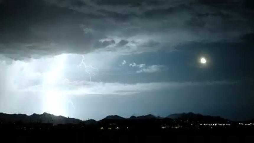Thunder in a dark sky with full moon and city lights glowing
